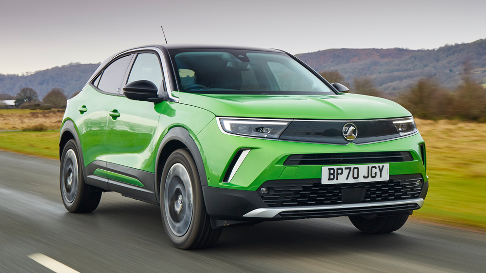 A bright green Vauxhall Mokka cruises down a country road with forests in the distance